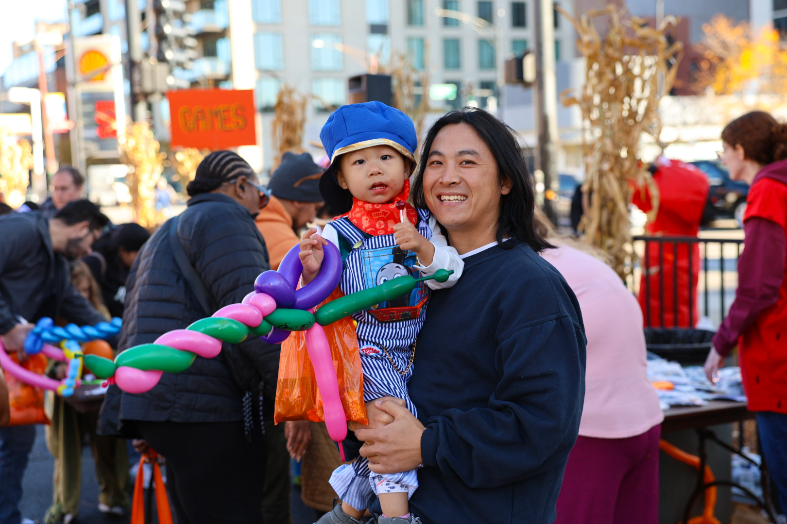 Man holding a toddler at a street festival with colorful balloon shapes in the foreground.
